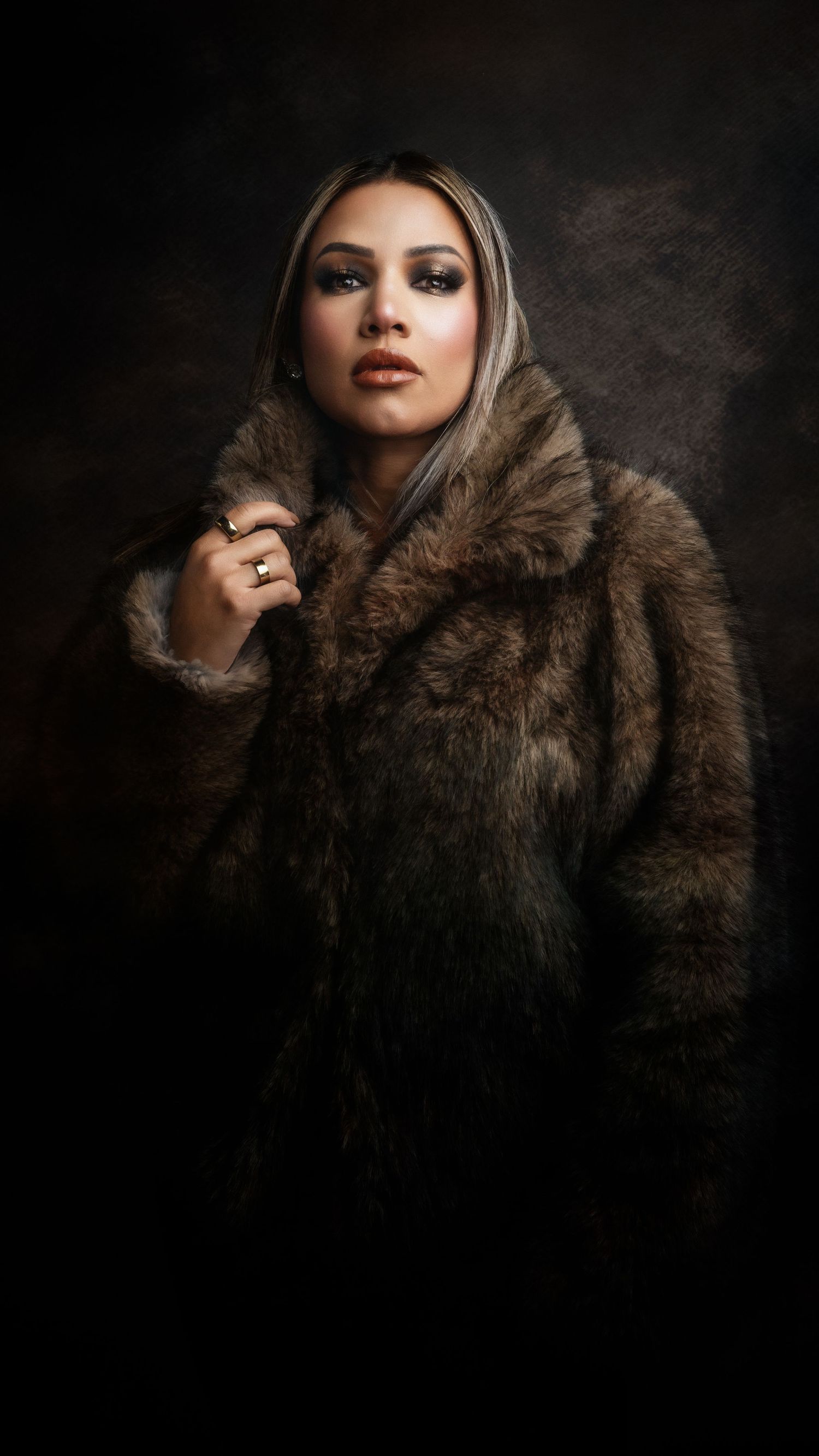 Woman in luxurious brown fur coat posing dramatically against dark background in elegant portrait photography.