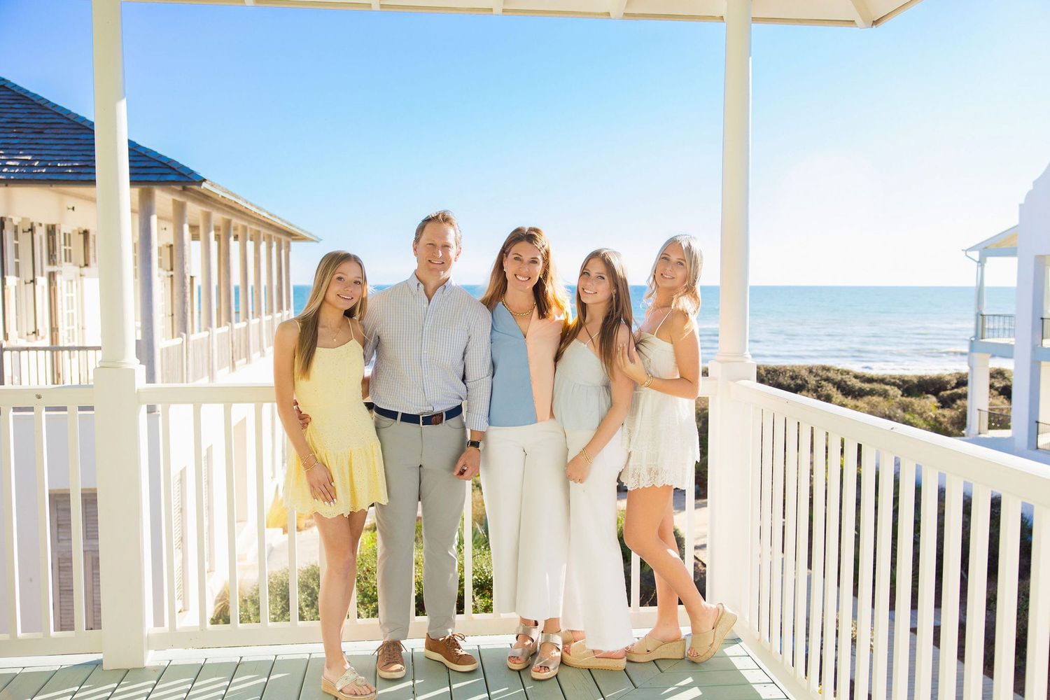 Family of five smiling on a beachfront porch in summer outfits with ocean views.