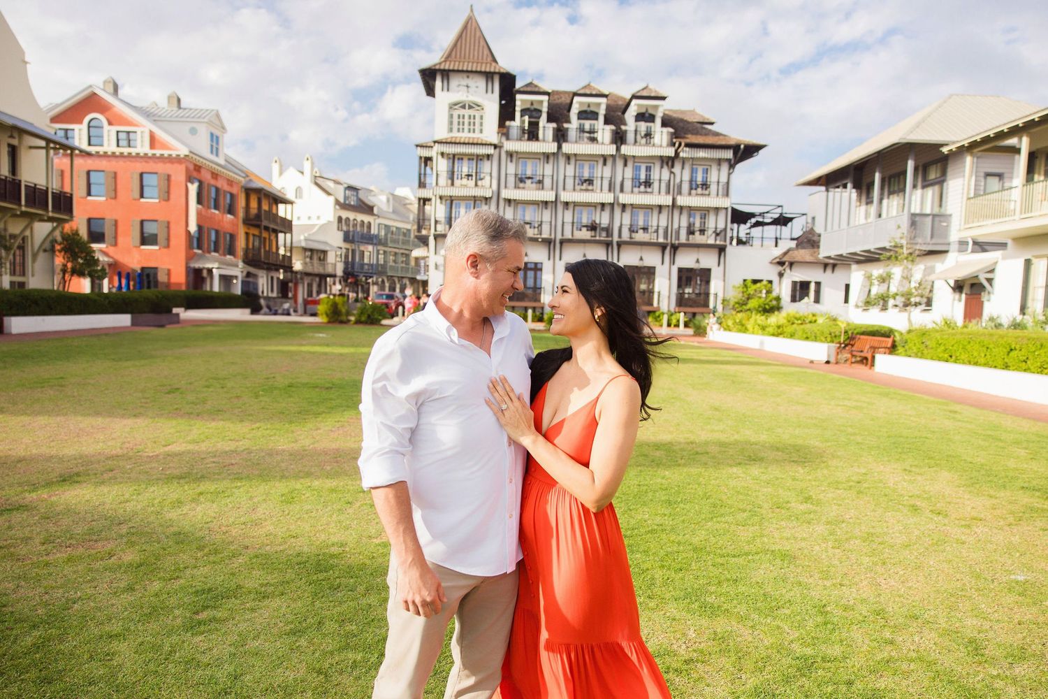 Couple sharing a romantic moment on a green lawn with colorful historic buildings behind them.