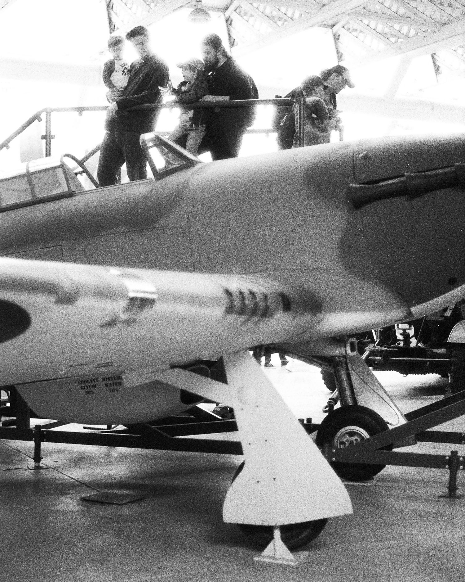 Black and white photo of a vintage WWII fighter aircraft in a hangar with people examining the cockpit.