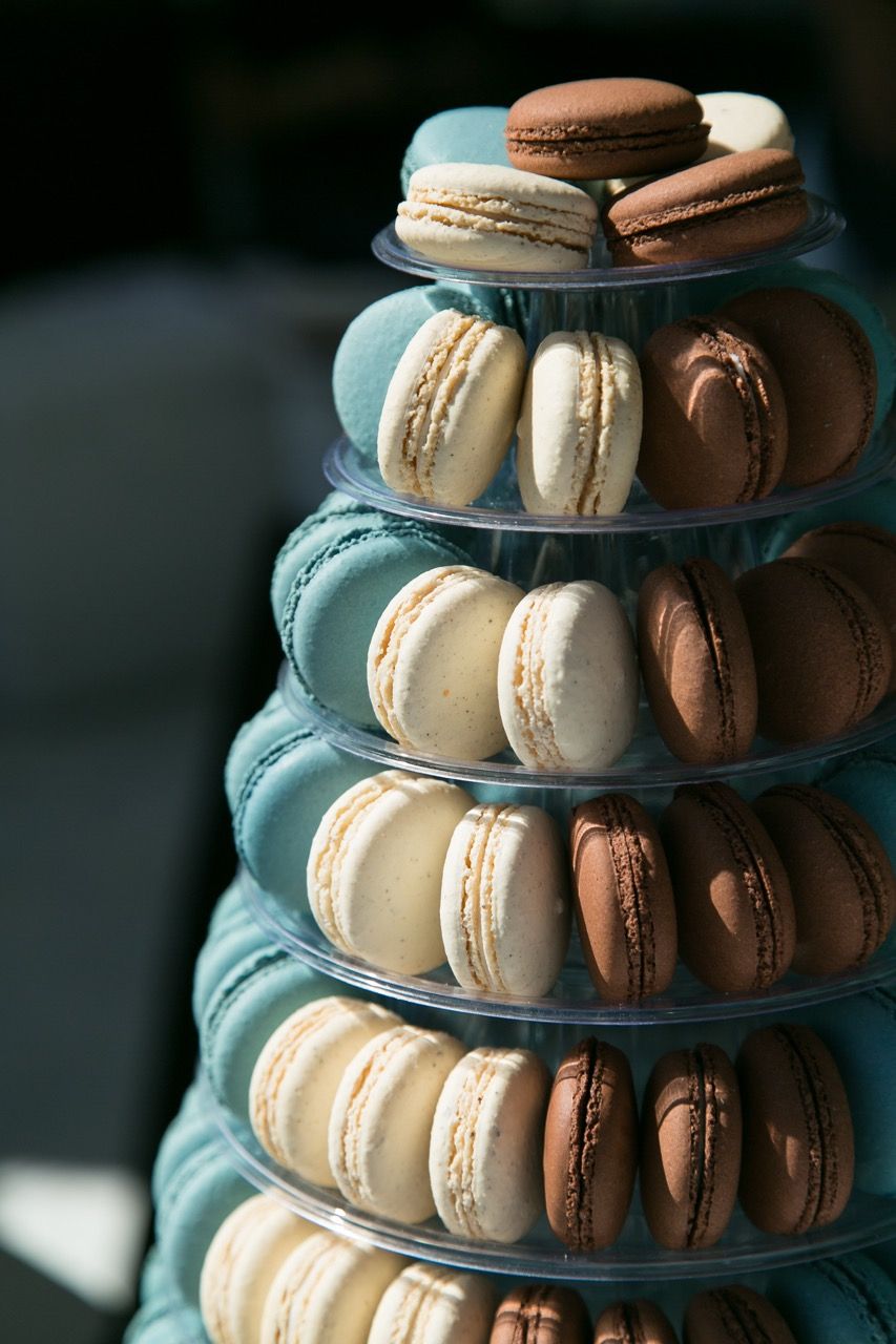 Elegant macaron tower display with teal, white, and chocolate brown French macarons arranged on tiered plastic stands.