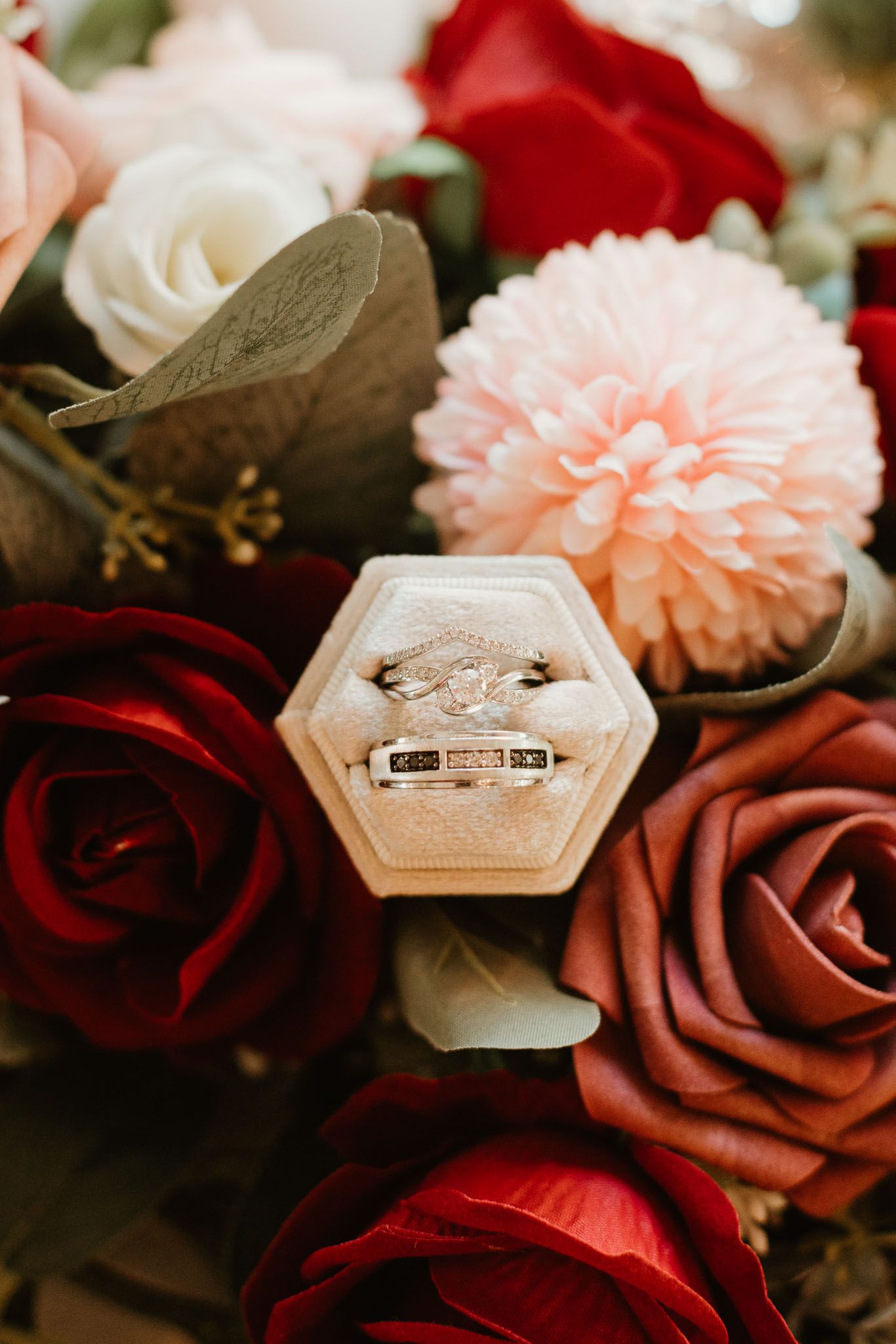 Diamond engagement ring and wedding band in hexagon velvet box surrounded by red and pink roses.