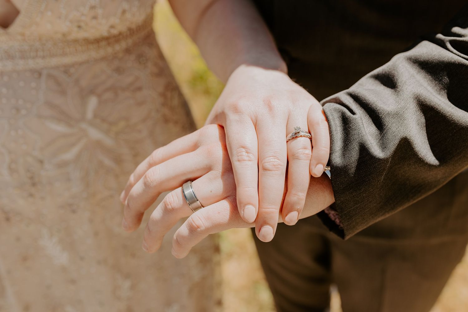 Newlywed couple displaying matching wedding bands on their hands, bride in lace dress and groom in gray suit at Lake Cuyamaca, Julian.