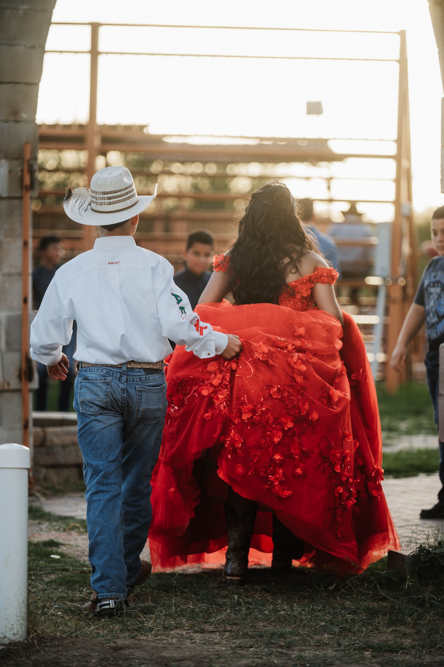A couple in western attire walking together with her wearing a flowing red formal dress at sunset.