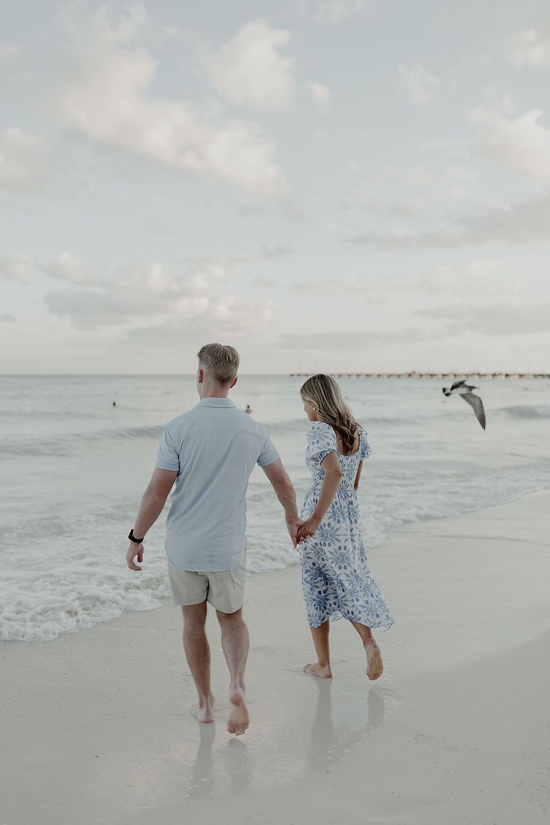 Couple holding hands and walking along the shoreline during a romantic beach photoshoot in Tulum.