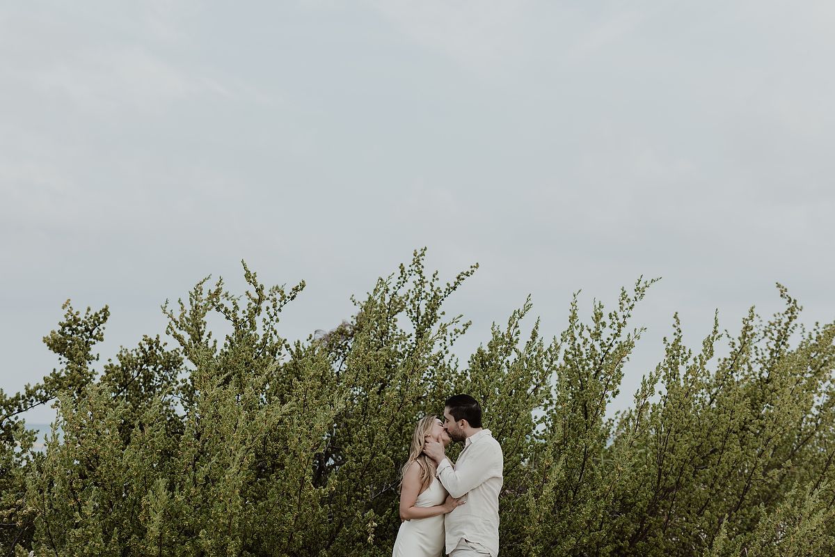 Engaged couple sharing an intimate kiss surrounded by greenery during a luxury portrait session in Tulum.
