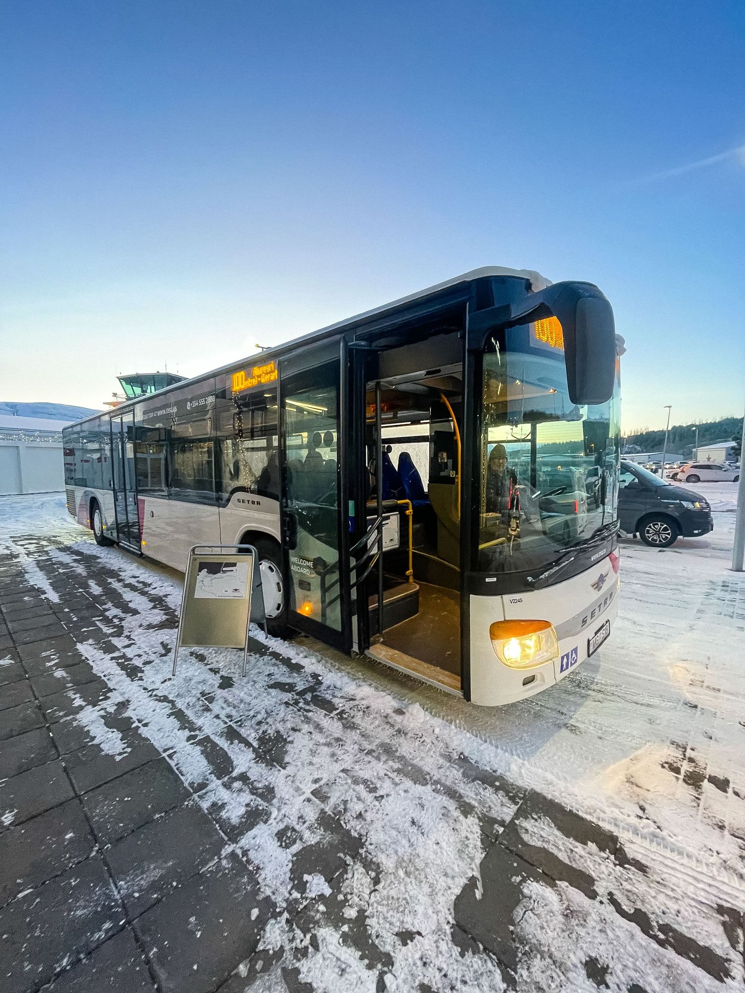 Public transport bus stationed in snow-covered lot with mountains in distance.