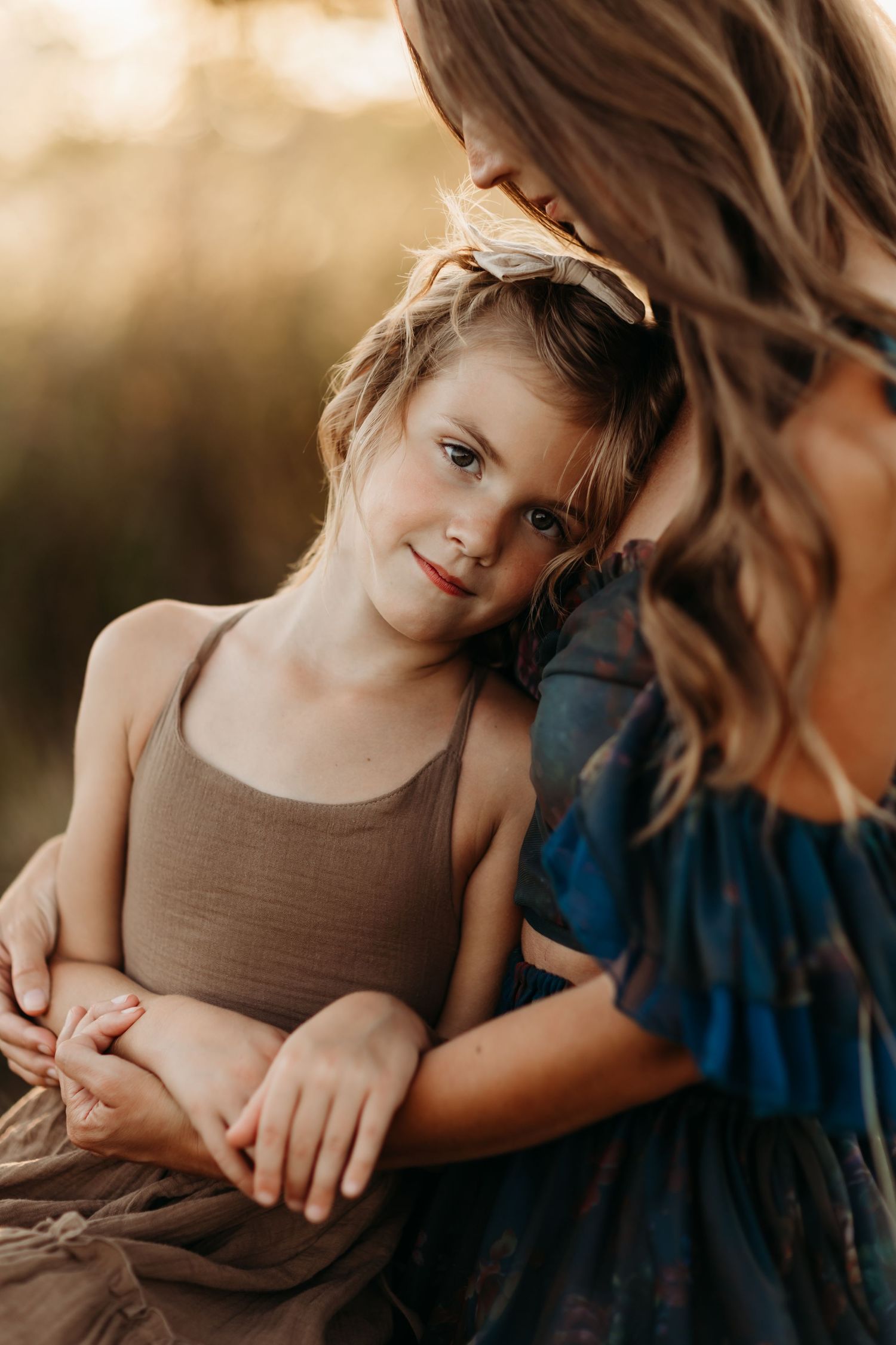 A warm sunset portrait of a parent and child sharing an intimate moment outdoors in neutral earth-toned clothing.