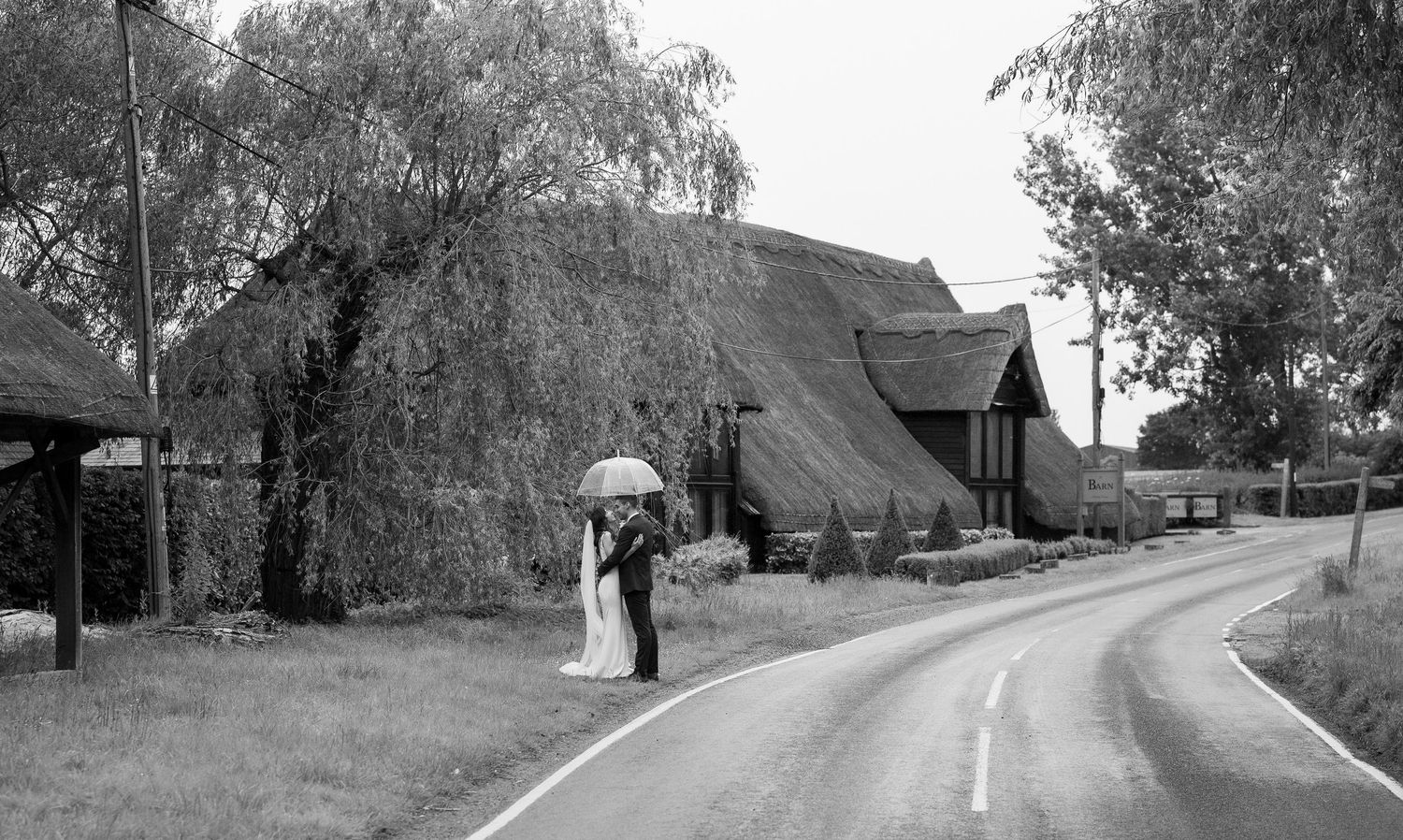 A romantic couple walking with a clear umbrella on a winding country road in black and white photography.