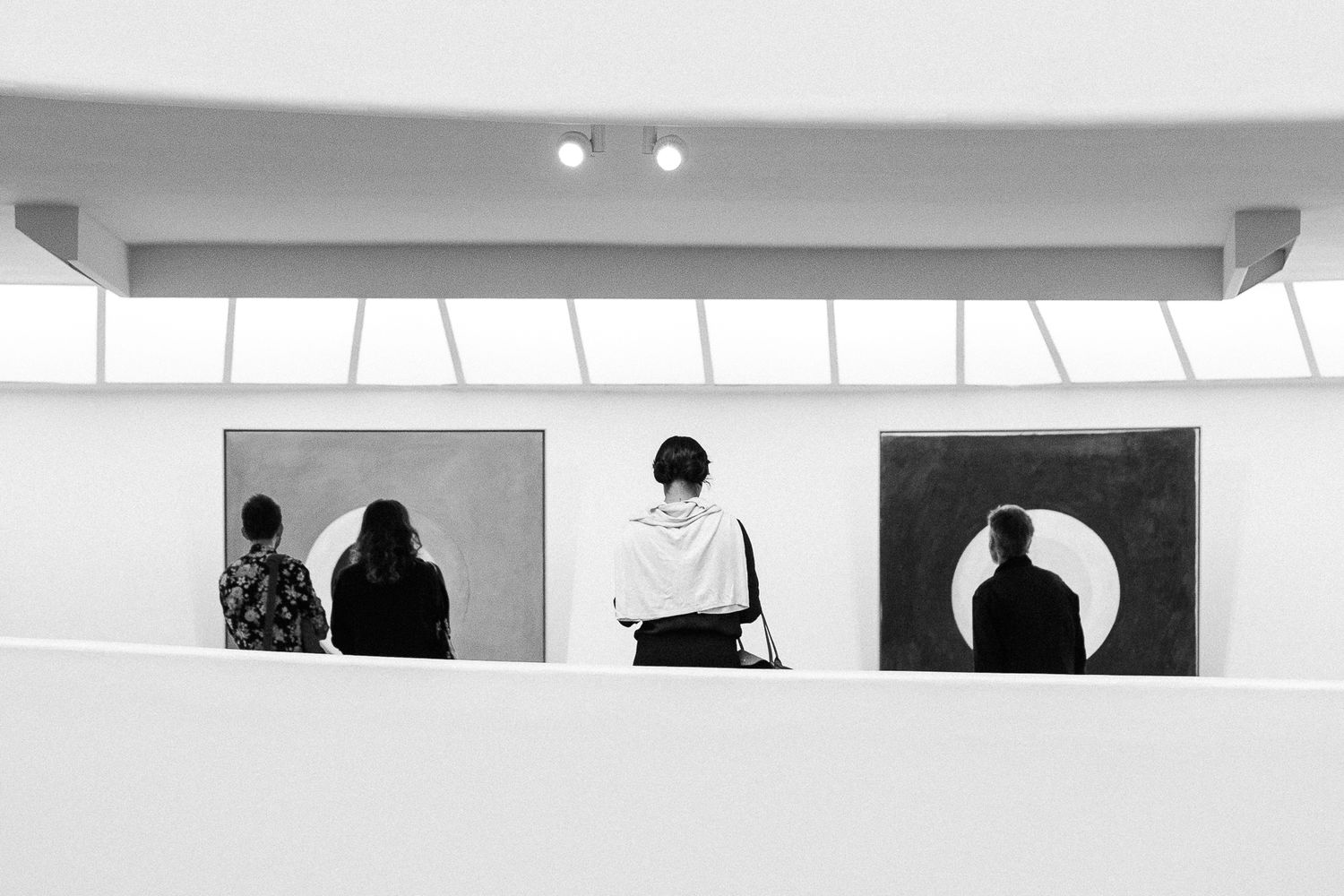 Minimalist gallery space with silhouetted figures viewed through rectangular window openings.