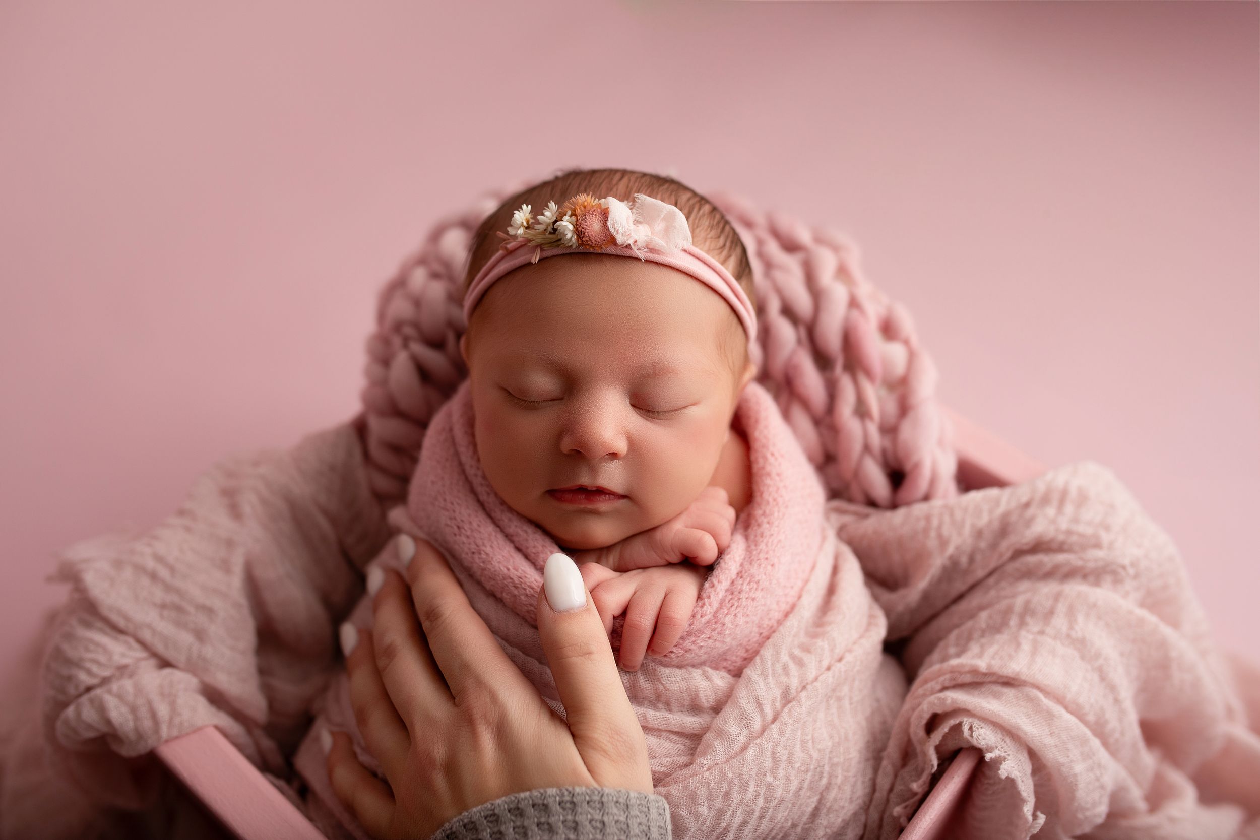 A peaceful sleeping newborn wrapped in soft pink and cream blankets rests in various gentle poses.