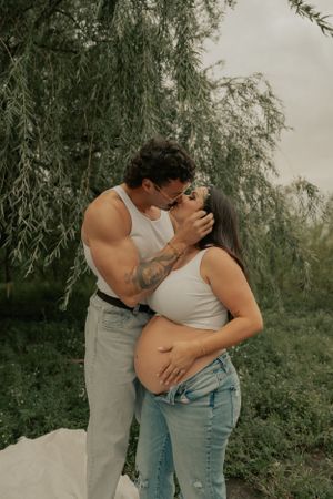 An intimate maternity photo with a couple sharing a tender moment under willow branches.