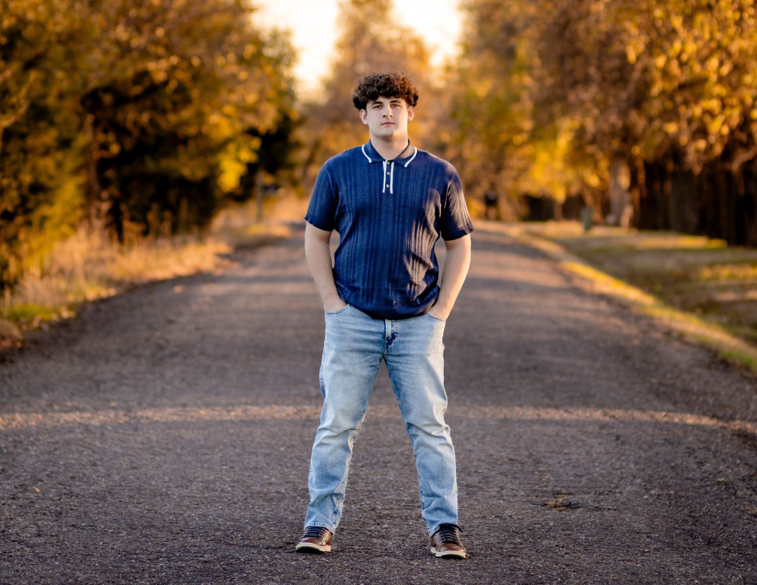 Person standing on a path surrounded by autumn trees in golden sunlight.