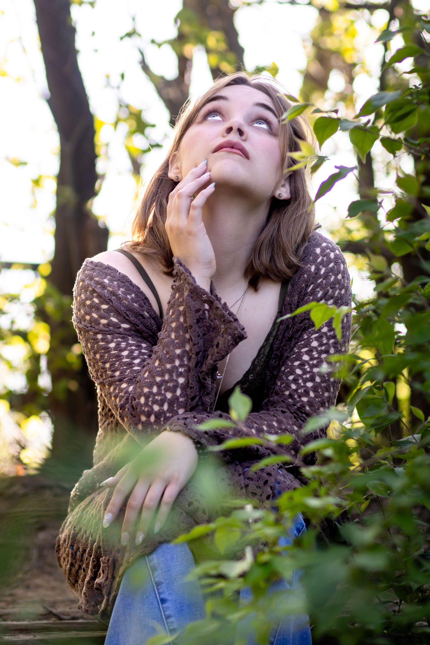 Profile portrait of person in polka dot shirt looking up contemplatively among tree branches and green foliage in sunlight.