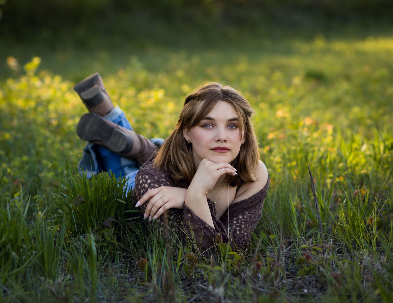 A person lying in a flowery meadow on a sunny day wearing casual attire and looking contemplative.