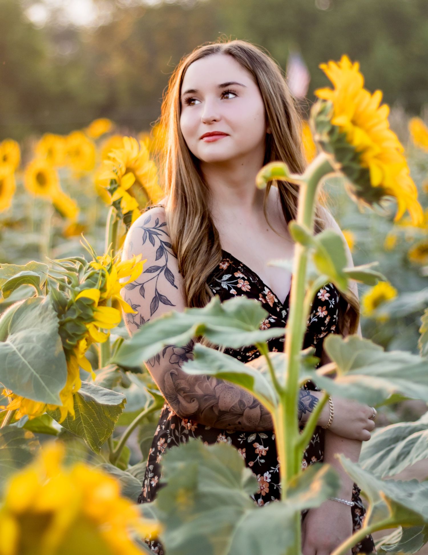 A dreamy portrait in a vibrant sunflower field shows a person in a floral dress looking wistfully into the distance.