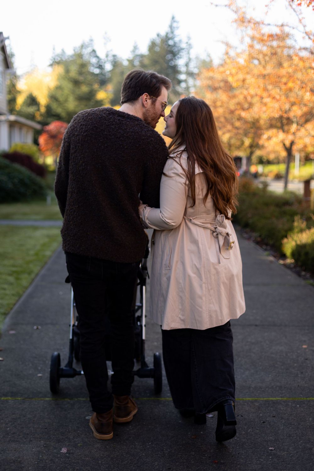 Couple standing with stroller on walkway surrounded by fall foliage.