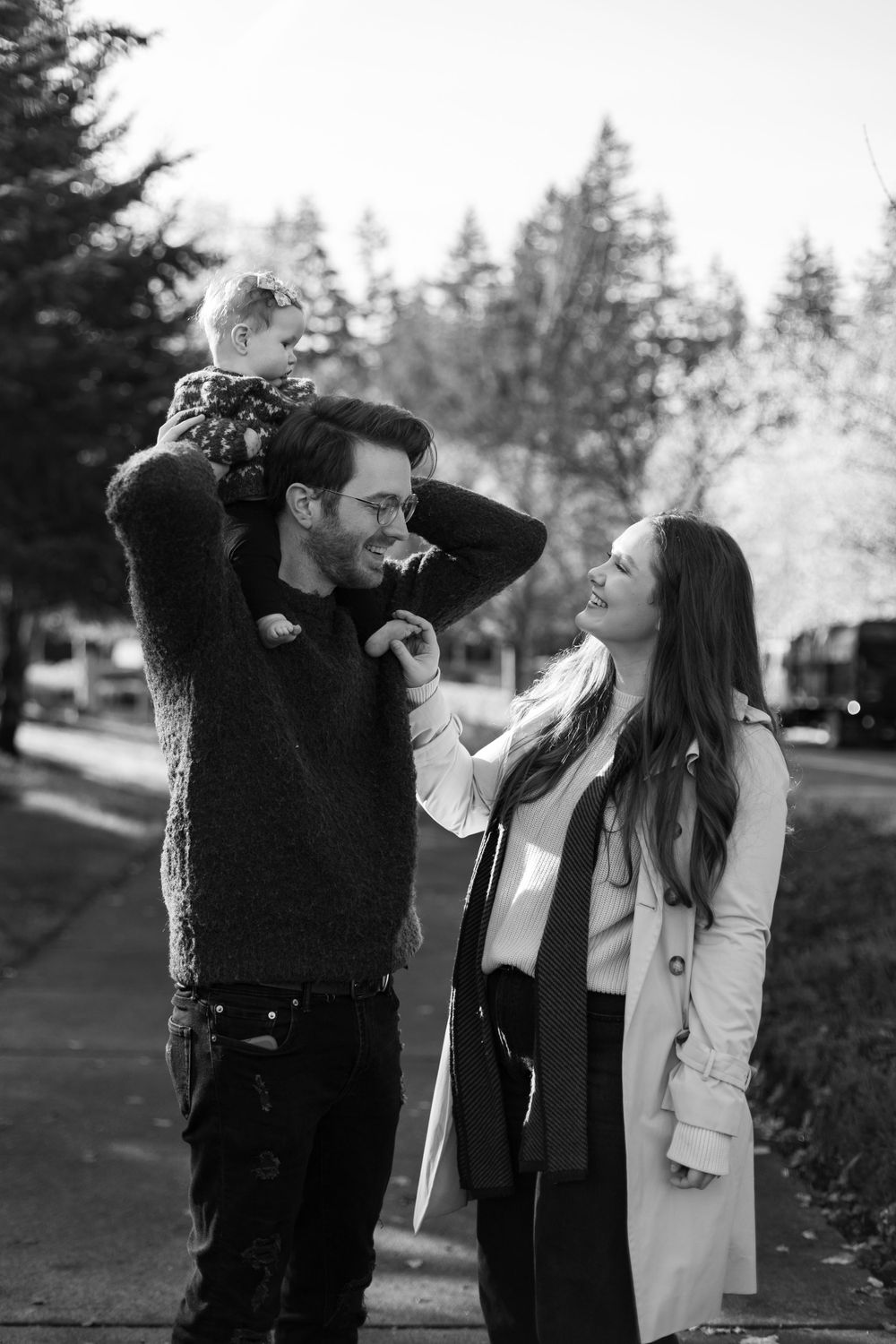 Black and white photo of a playful family moment outdoors with evergreen trees in background.