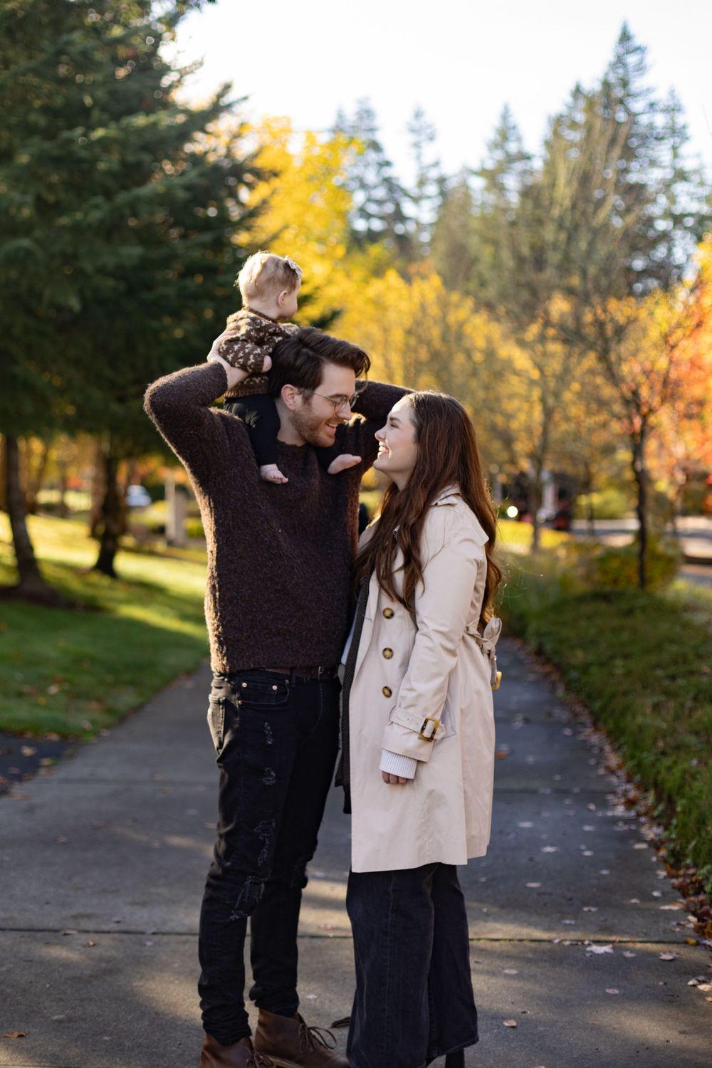 Family enjoying a tender moment on pathway with autumn trees in background.