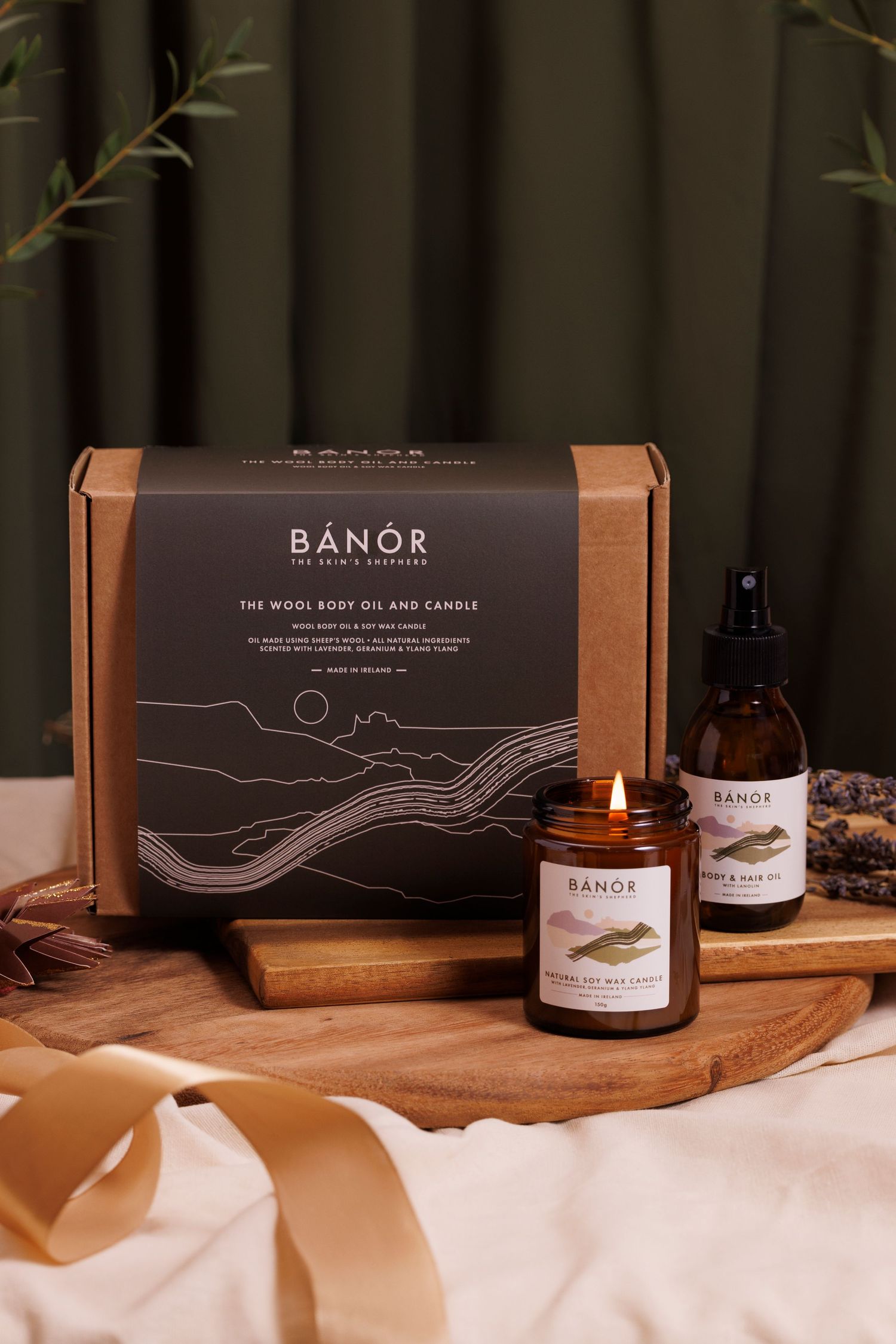 Banor luxury gift set featuring candle and oil products in elegant brown packaging on wooden surface, fabric backdrop and gold ribbon.