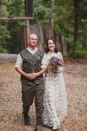 A couple poses on a woodland path with rustic wedding attire.