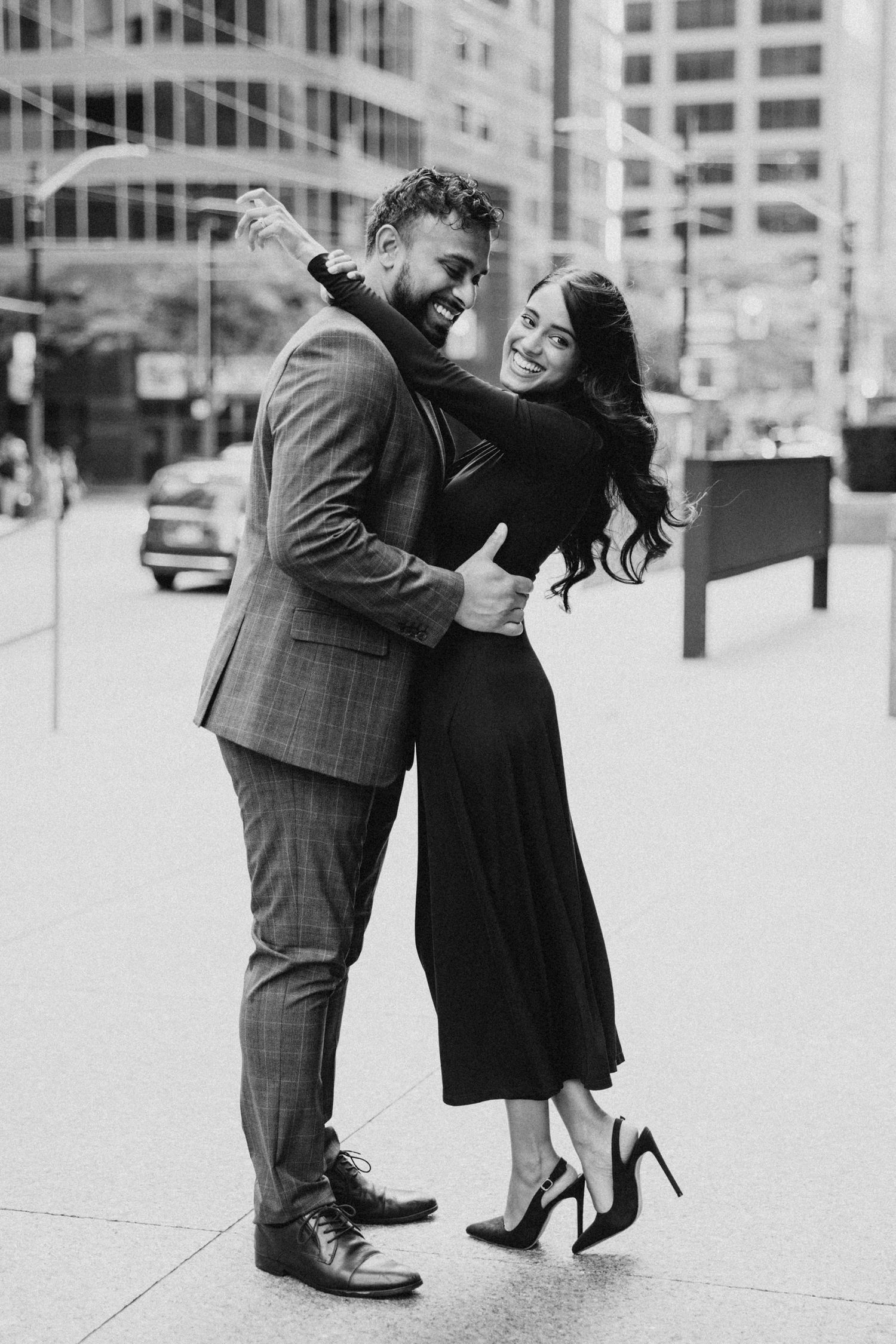 A couple in formal attire shares a romantic dance moment on a city sidewalk with buildings in the background.