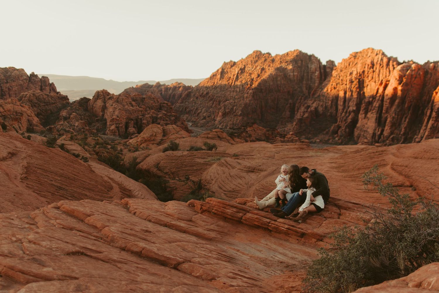 Couple sitting on red rock formation in snow canyon utah desert landscape at sunset.