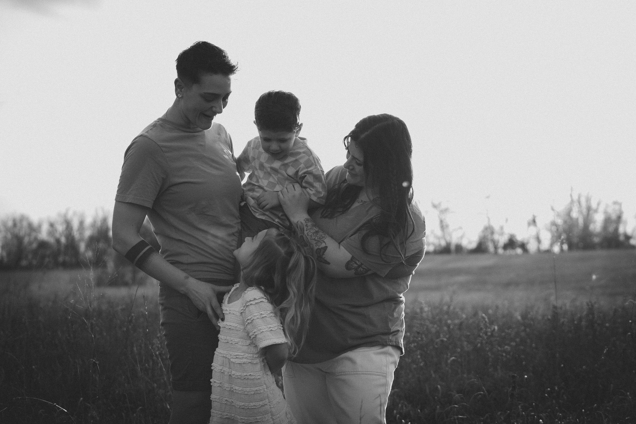 A family shares a tender moment together in a grassy field, captured in black and white photography.