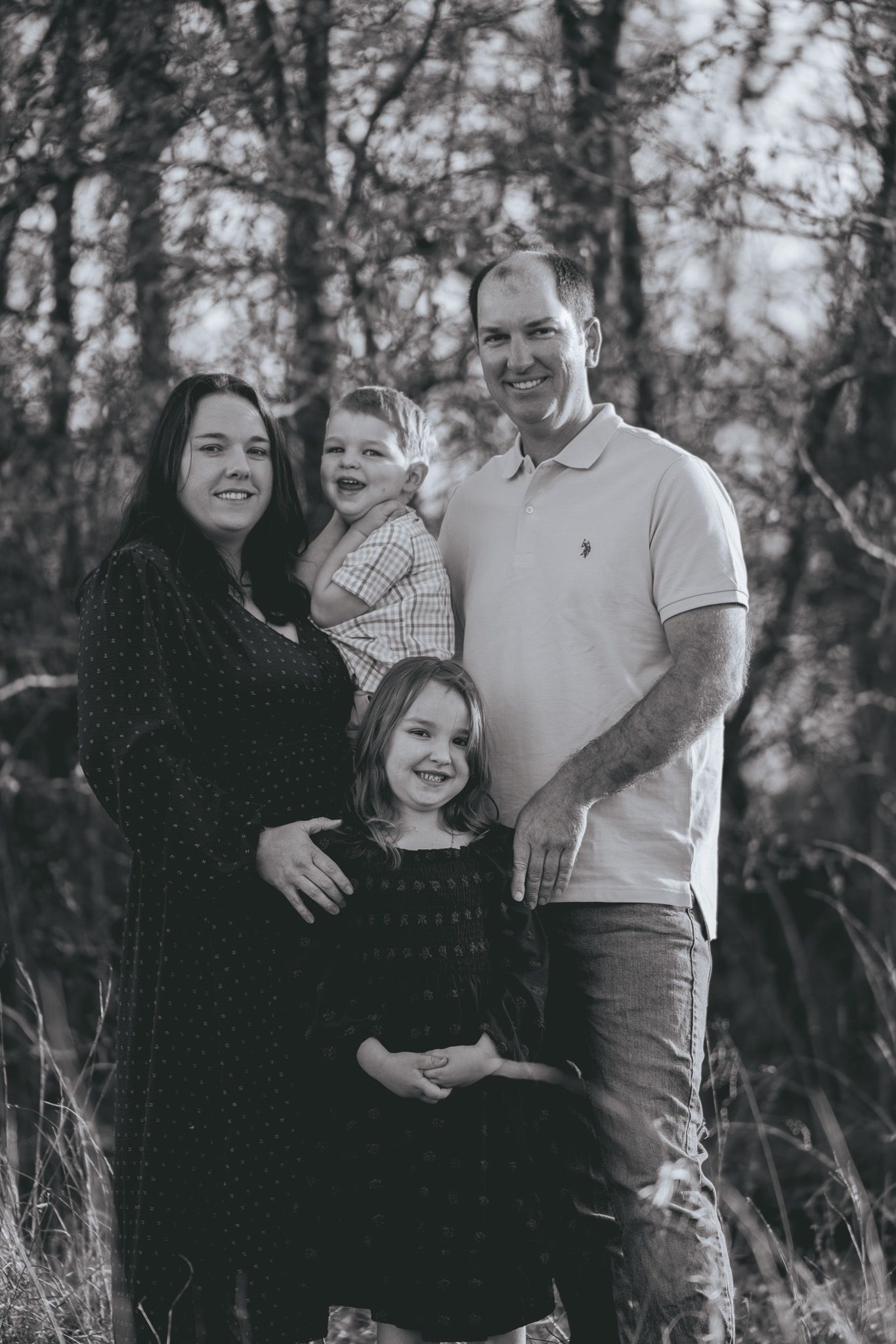 A family poses together outdoors in a natural setting with trees and foliage in the background.