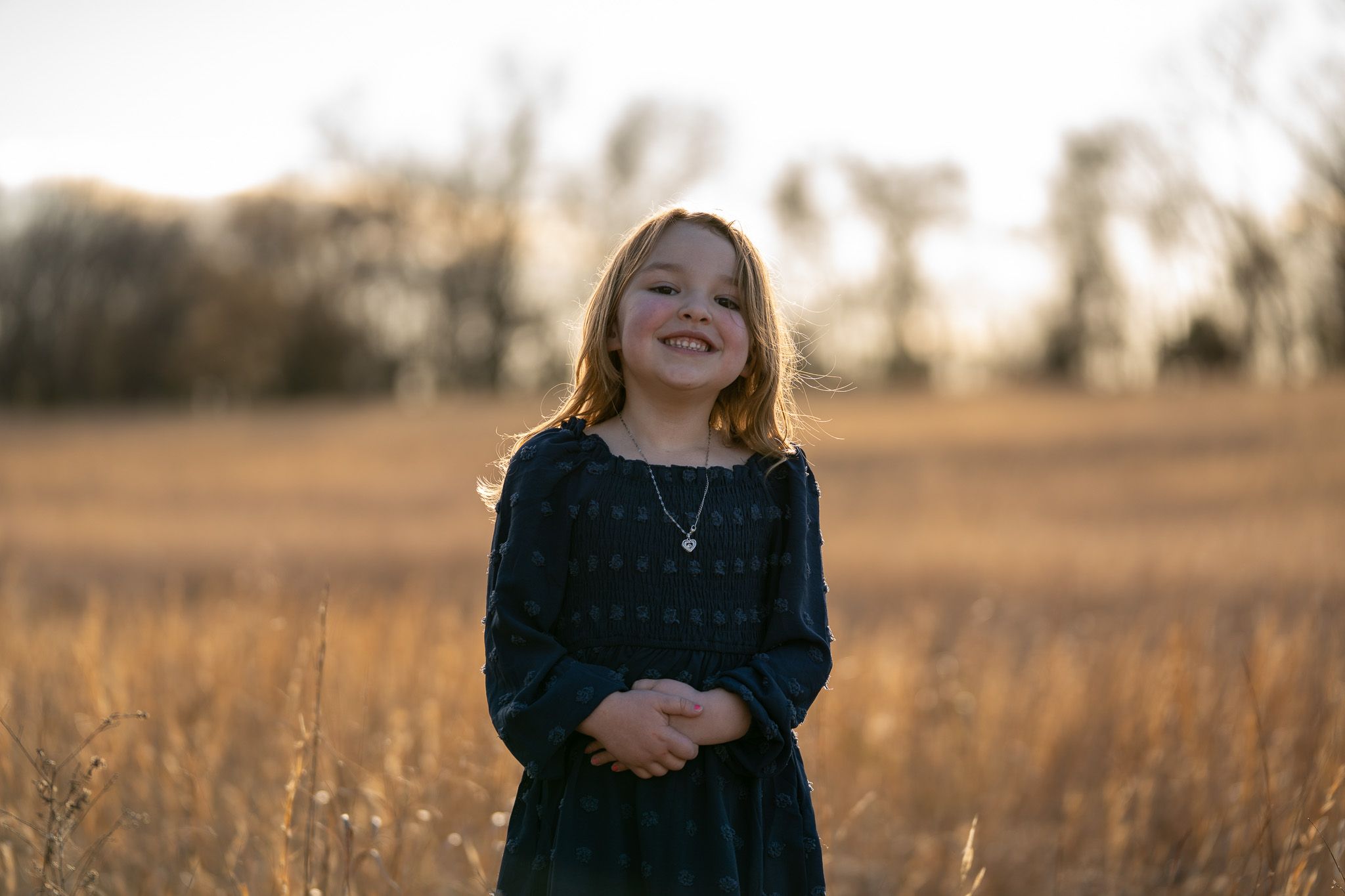 A person wearing a black sweater stands in a golden field during sunset with warm autumn lighting.