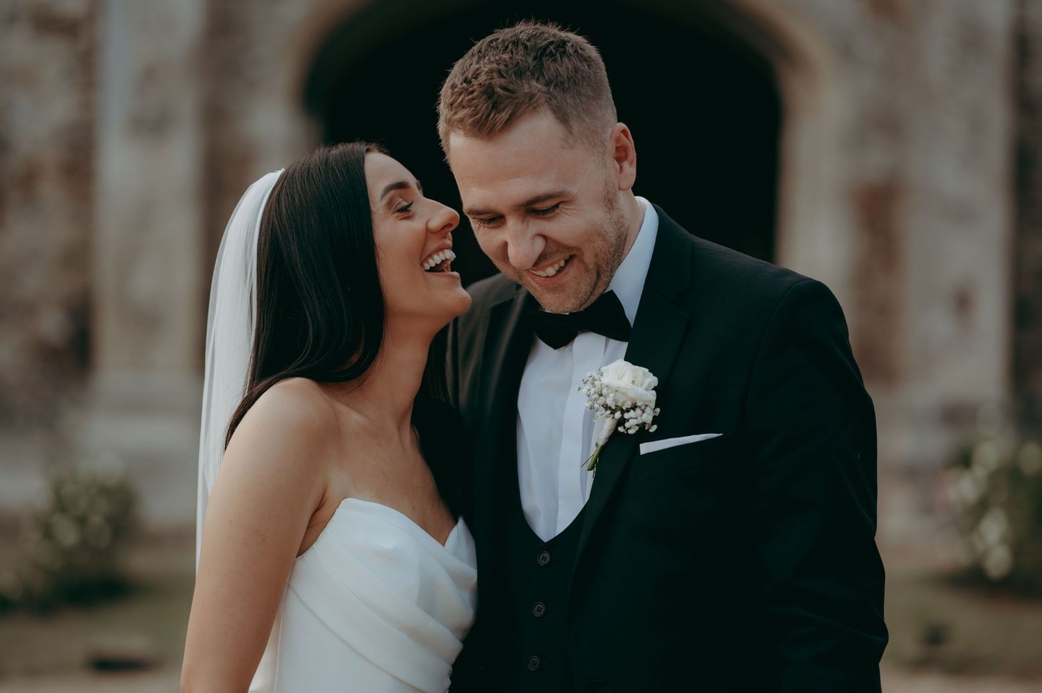 A joyful newlywed couple sharing an intimate candid moment together during their outdoor wedding photoshoot. Pentney abbey