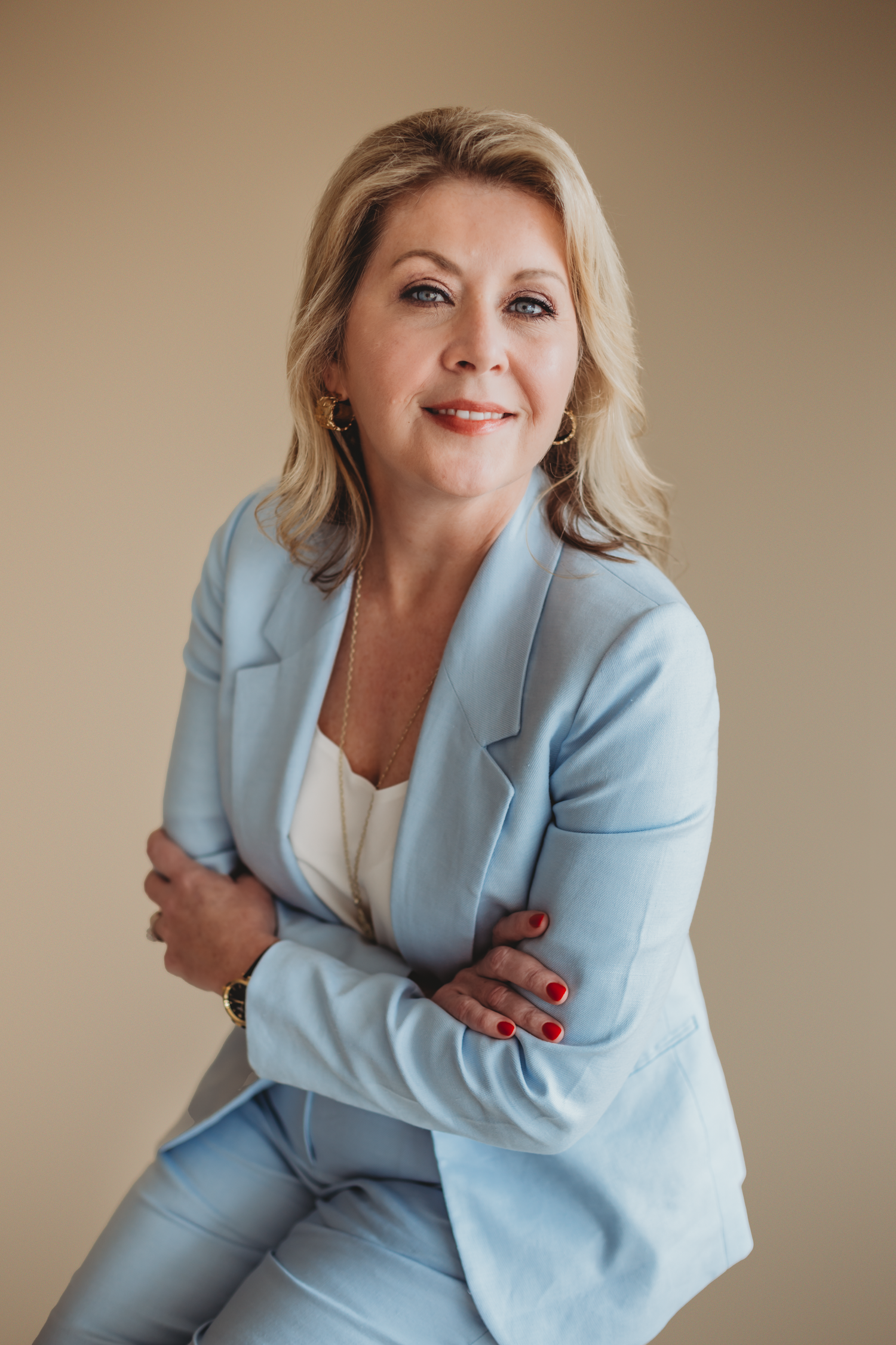 Middle aged blonde professional lady in blue matching suit poses for headshot in studio