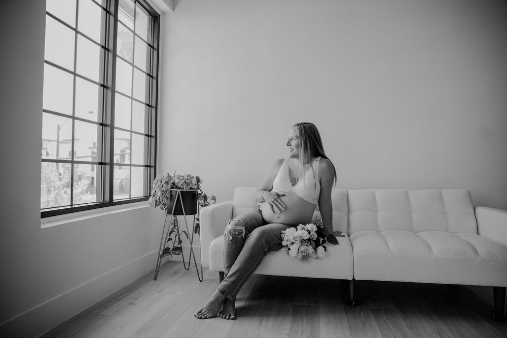 Black and white photo series showing different poses on a white tufted couch near large windows in a studio setting.