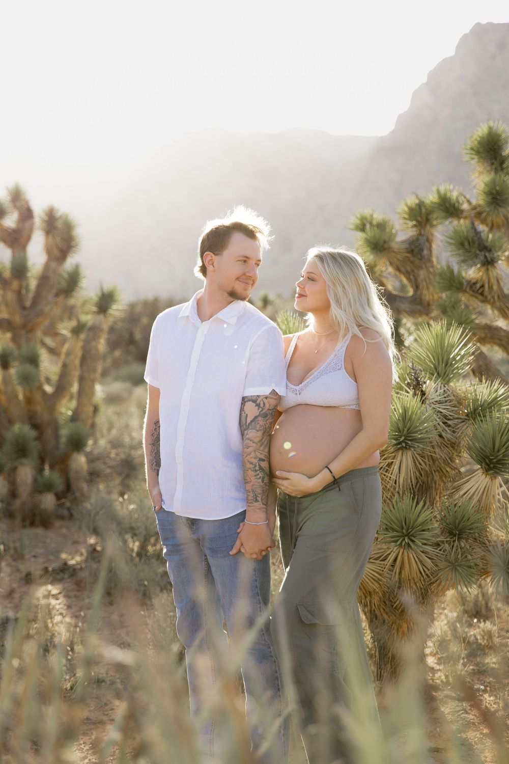 A couple shares romantic moments in a desert landscape with Joshua trees at sunset.