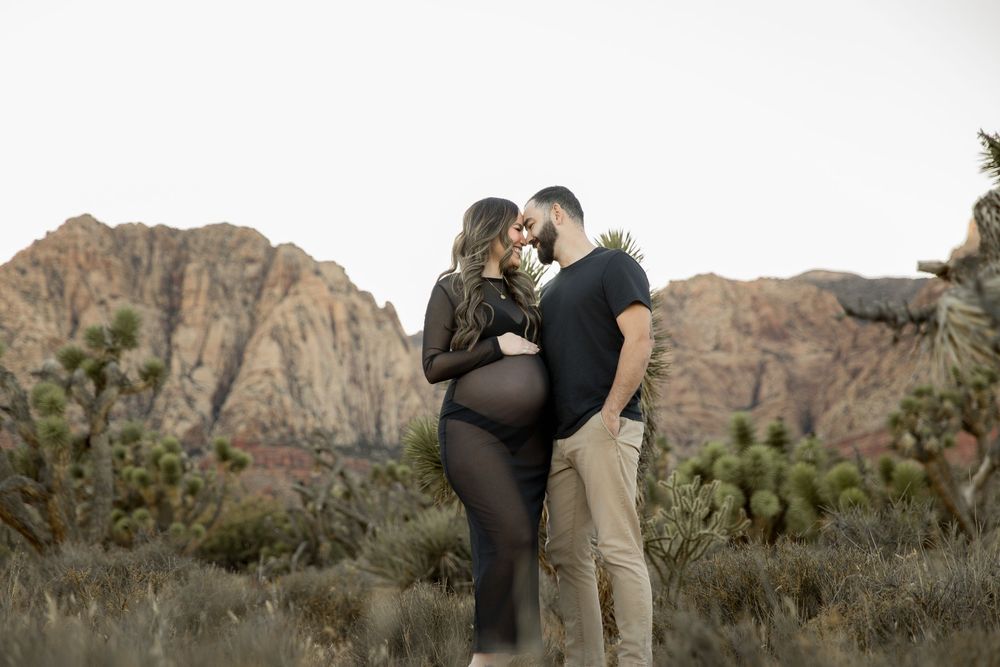 A couple shares a romantic moment against a backdrop of rugged desert mountains and desert flora at sunset.