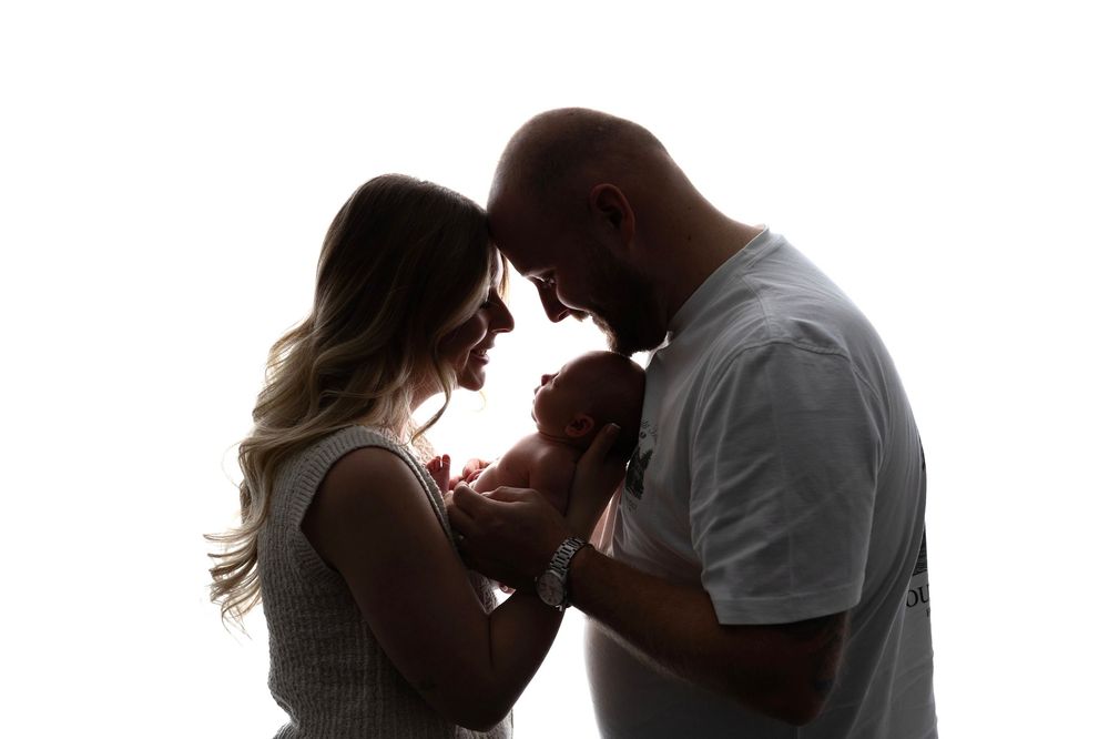 Silhouette of parents holding newborn baby against white background.