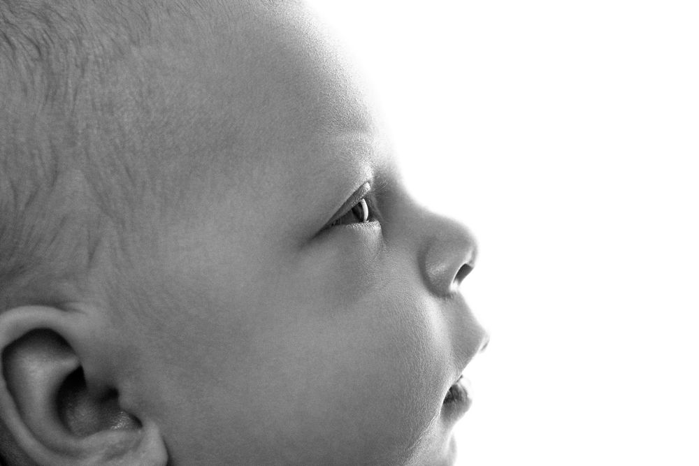 Black and white close-up profile portrait of a newborn baby looking up.