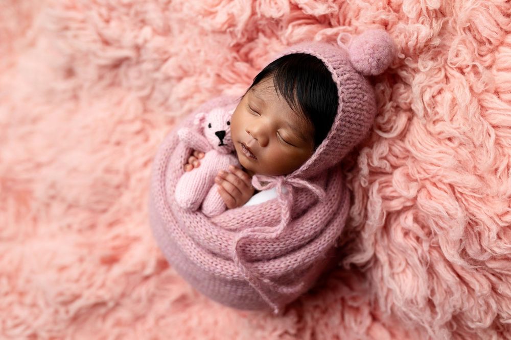 A newborn baby wrapped in soft pink blankets lies peacefully in a cozy setting.