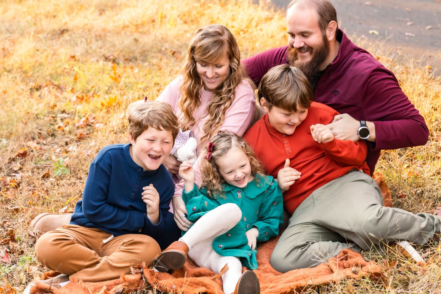 A family lies together on autumn leaves during a playful outdoor photo session in warm golden light.