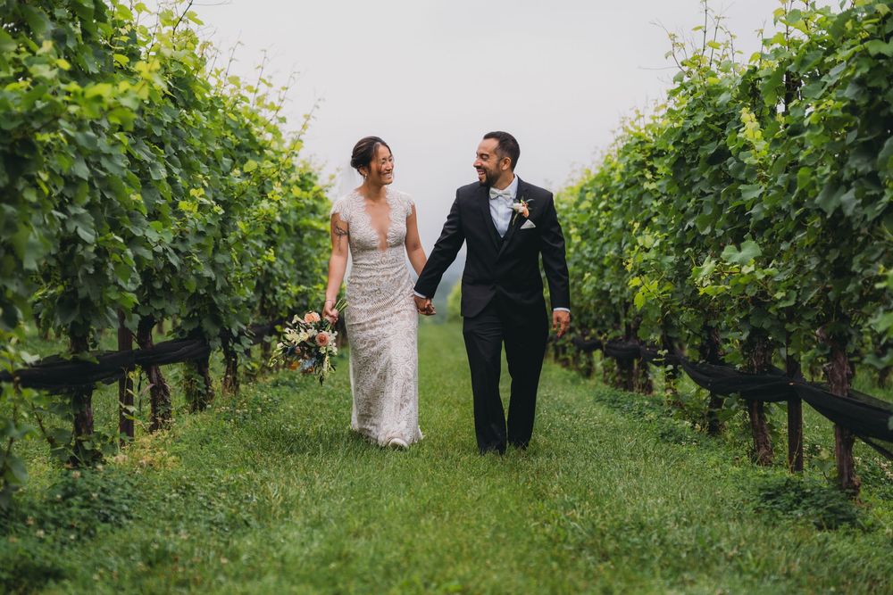 Bride and groom walking hand in hand through vineyard rows at Stone Tower Winery on their wedding day