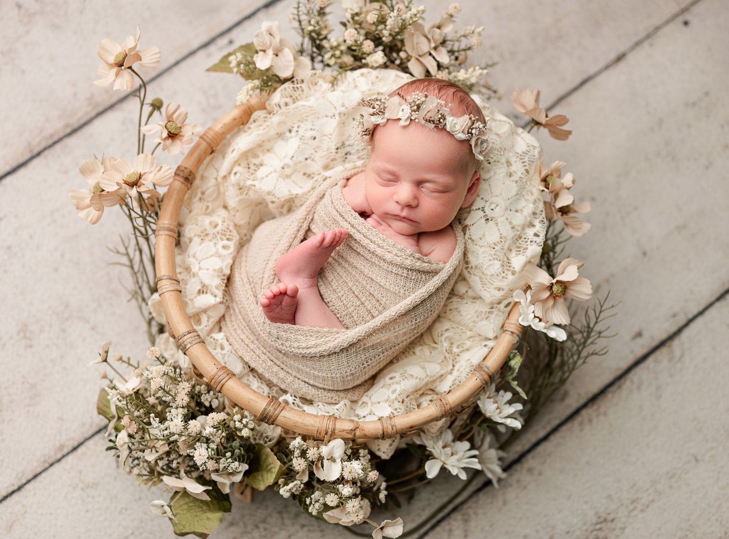 Newborn baby sleeping peacefully in a wooden bowl with lace and floral decorations for a professional photo shoot. Newborn Photographer
