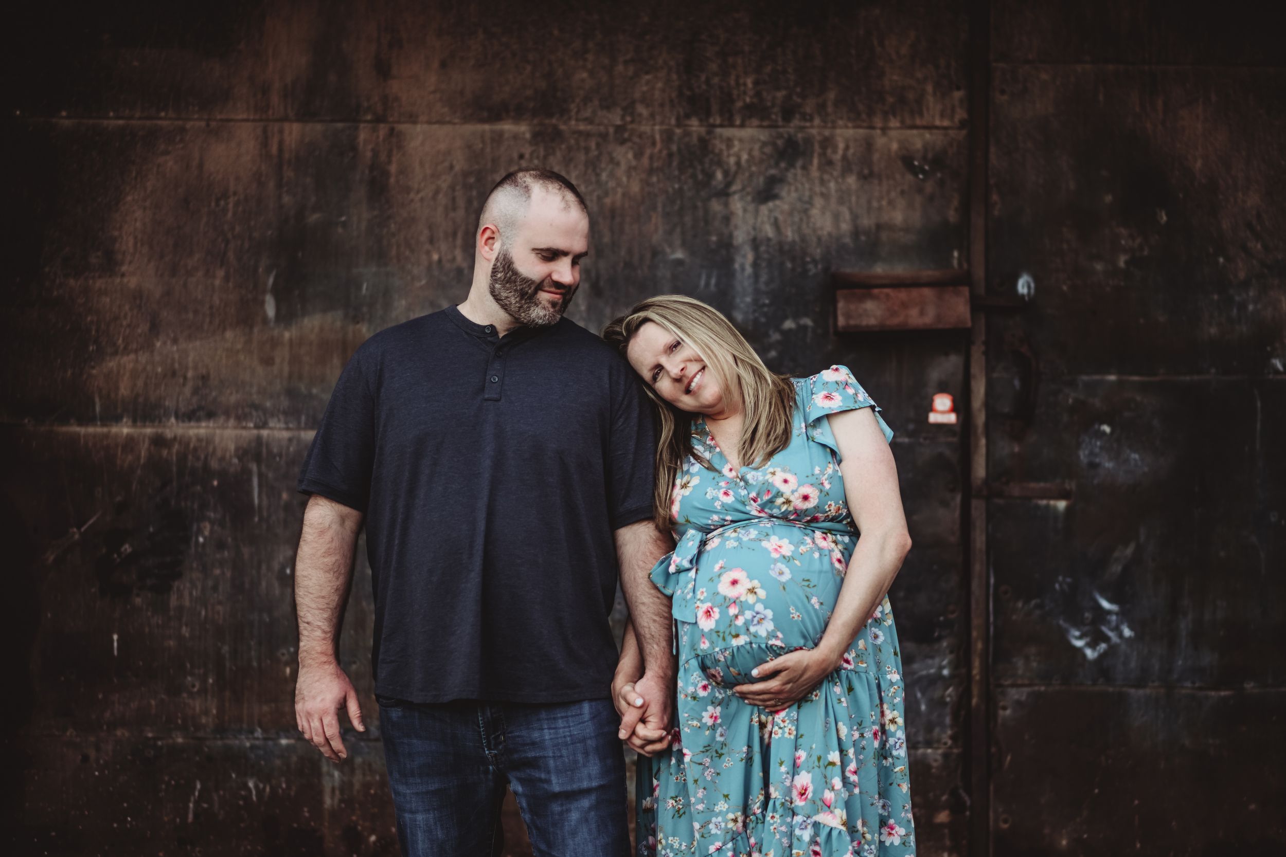 A maternity photo against an industrial backdrop with dark textured walls.