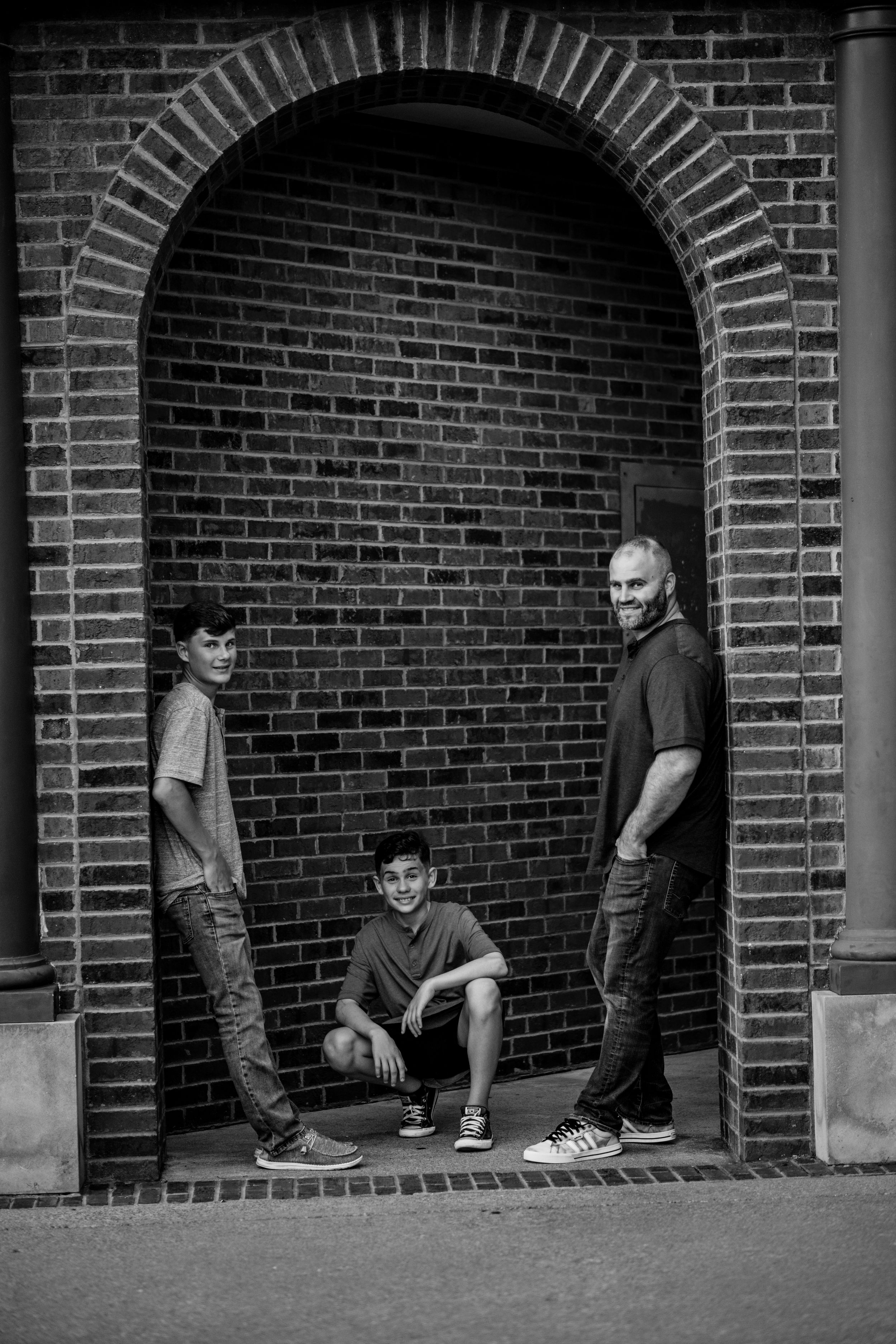 Black and white portrait of three people standing in a brick archway.