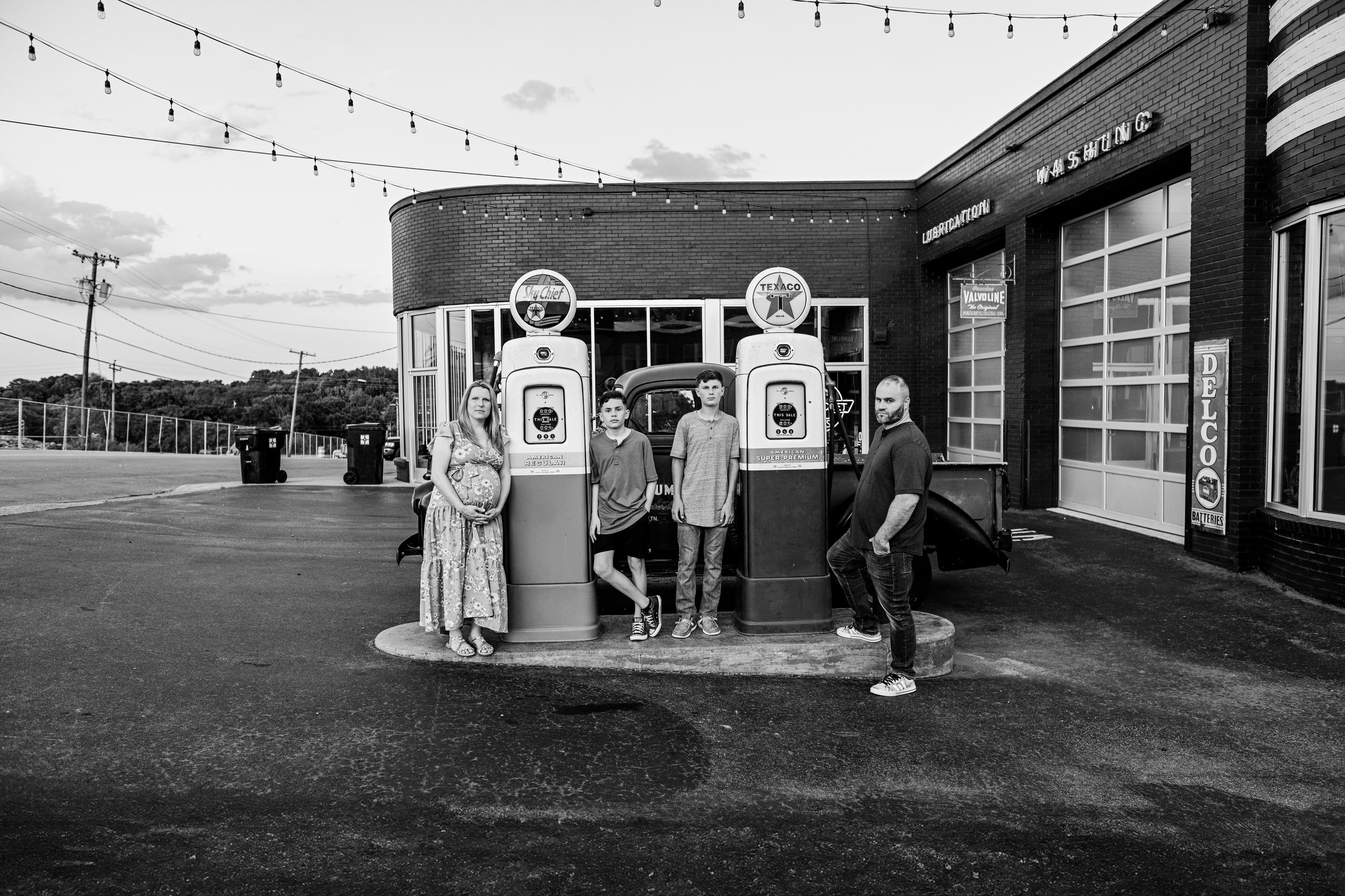 A black and white photo of people posing by vintage gas pumps at a retro station.