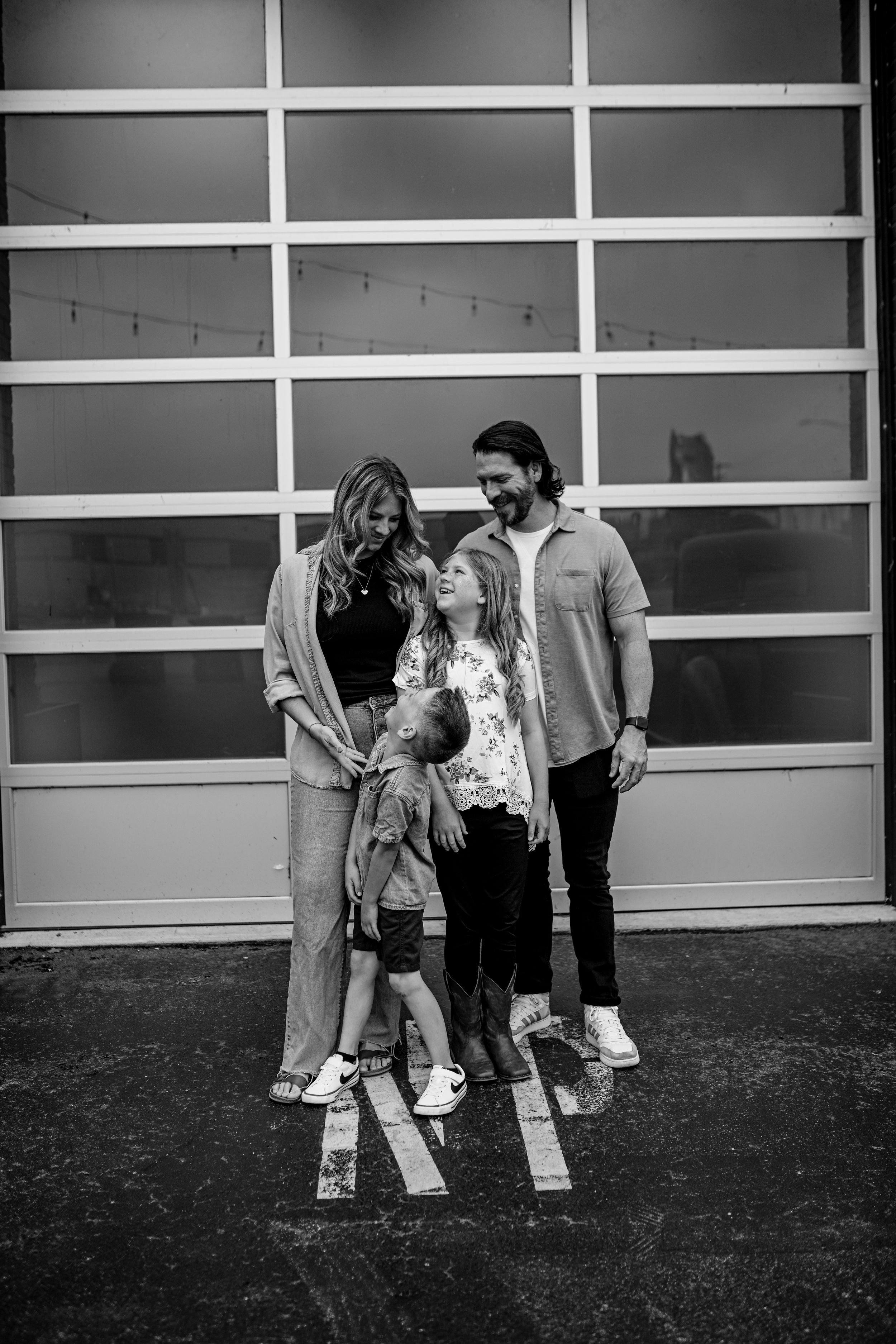 Family of four poses together against modern garage door backdrop in black and white.