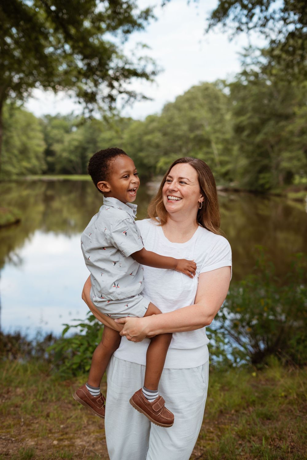 A joyful outdoor portrait by a serene pond showing loving interaction between parent and child.
