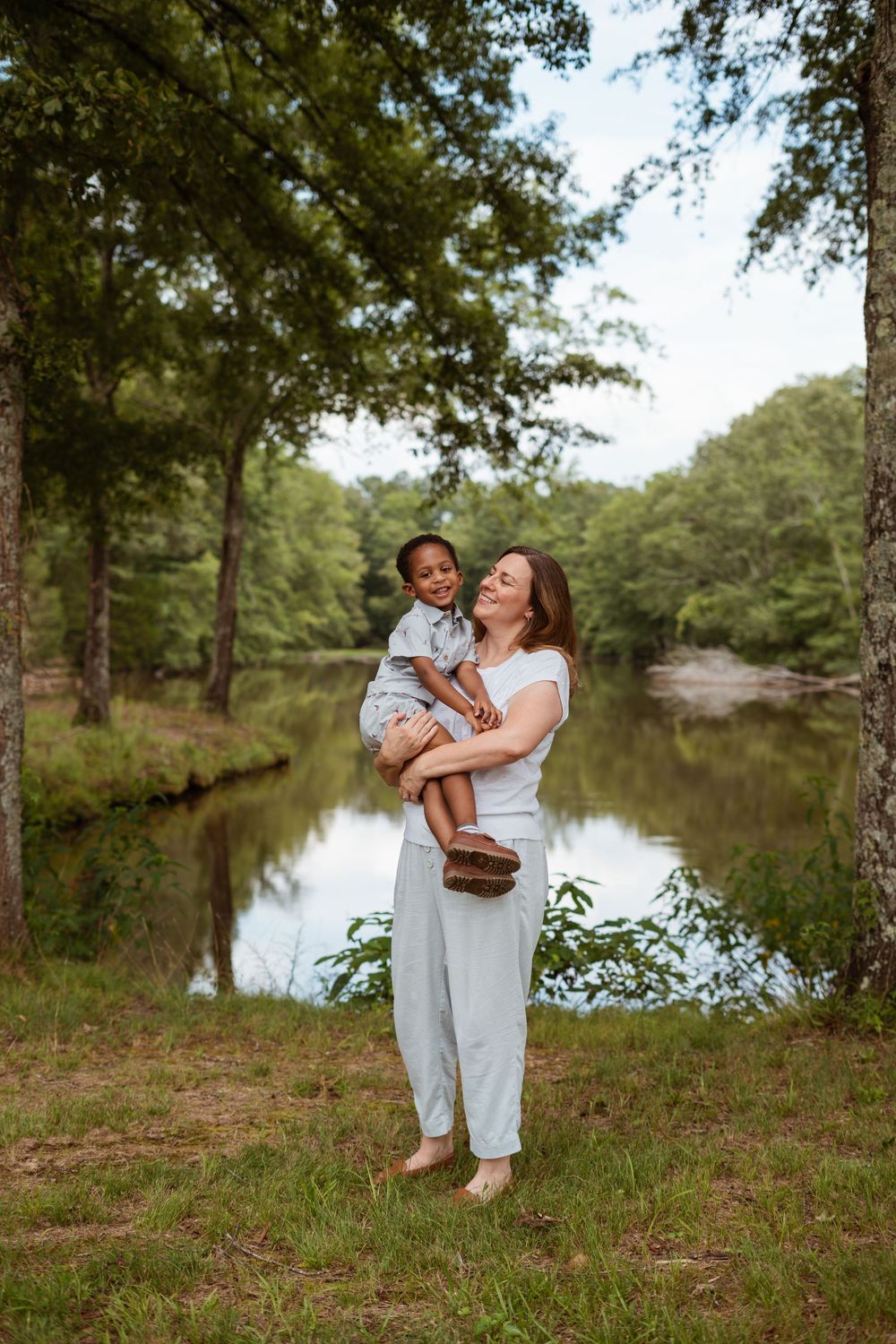 Candid family moment captured by a peaceful lake with trees in the background.