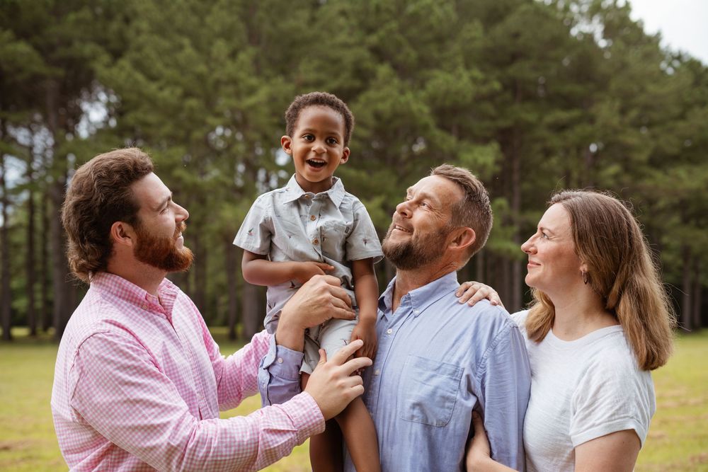Playful outdoor family photo showing group interaction against a forest backdrop.