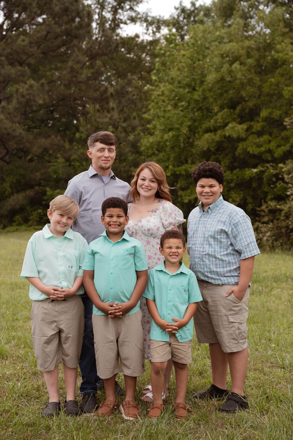Family group portrait of six people wearing coordinated outfits in an outdoor setting.