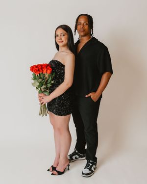 Couple in black outfits poses with red roses bouquet for formal portrait.